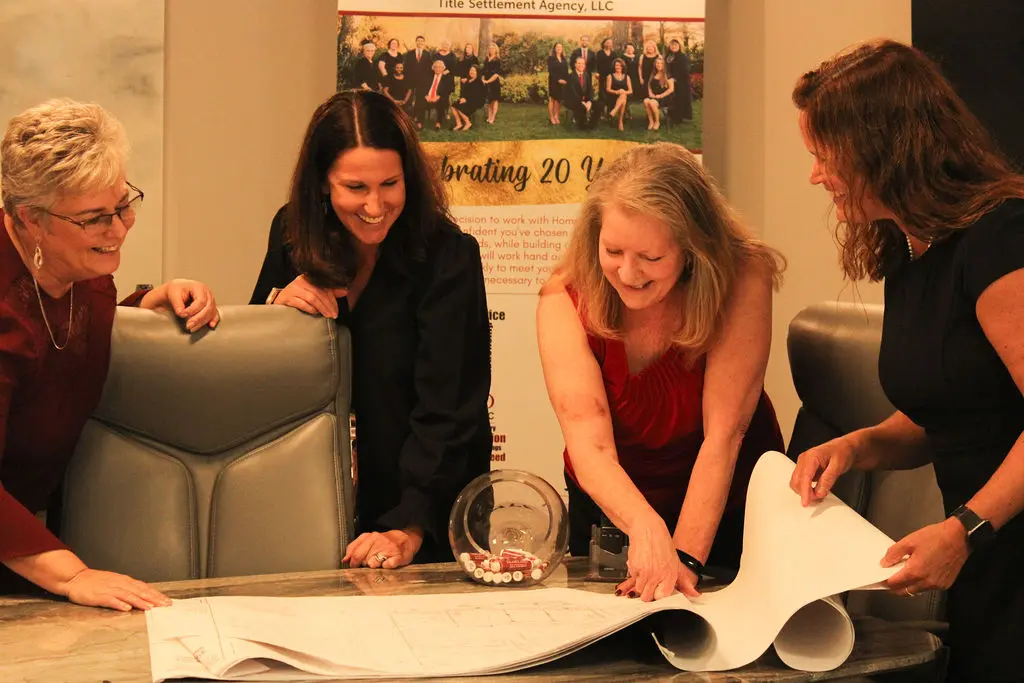 4 women gathered around a desk smiling and reviewing blueprints